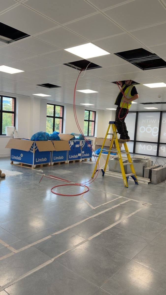 Engineer on a ladder running cables above the ceiling grid in a new office fit-out